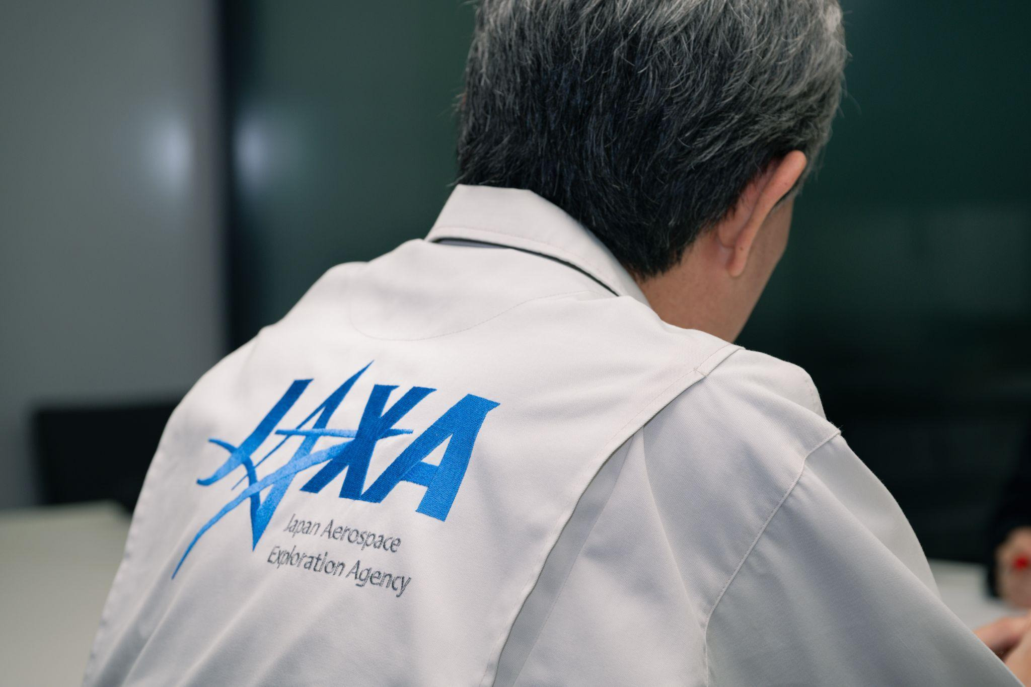 JAXAのロゴが入った作業着を着た澤井氏の後ろ姿